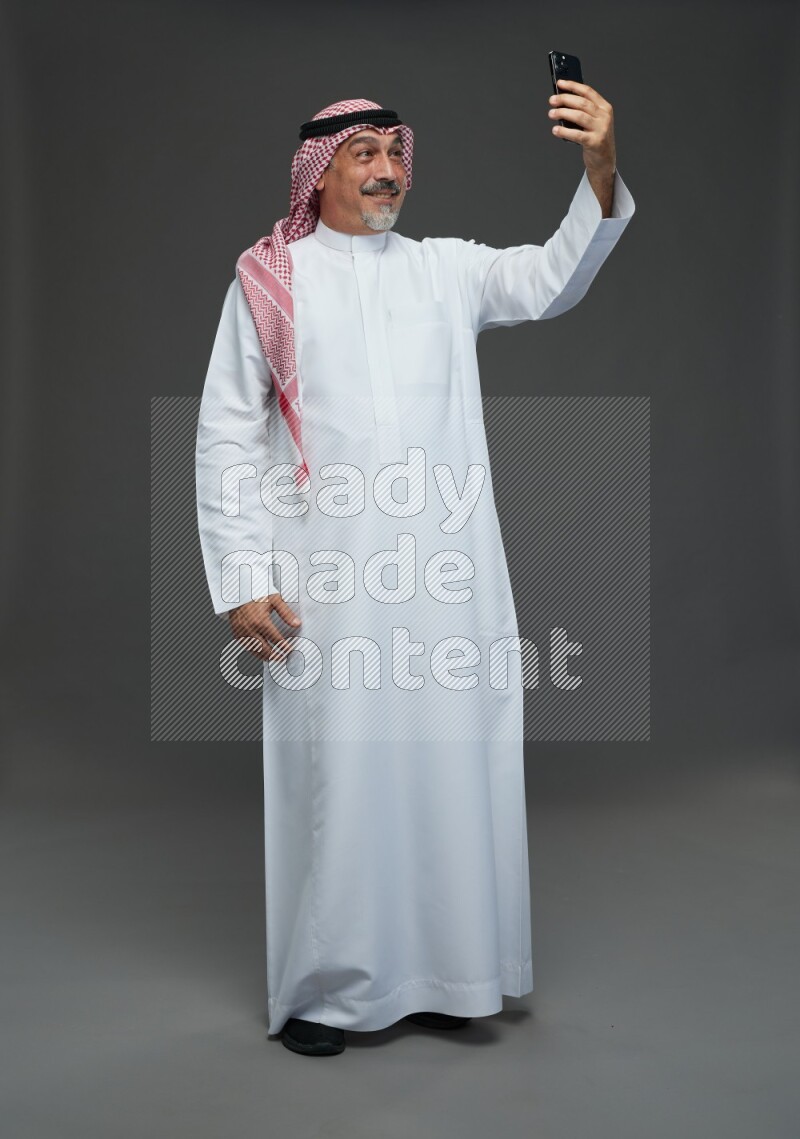 Saudi man with shomag Standing taking selfie on gray background