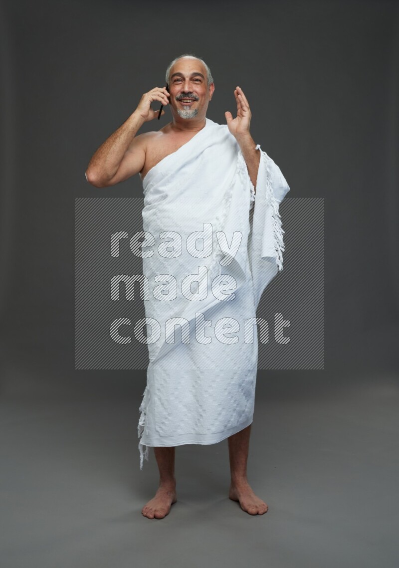 A man wearing Ehram Standing talking on phone on gray background