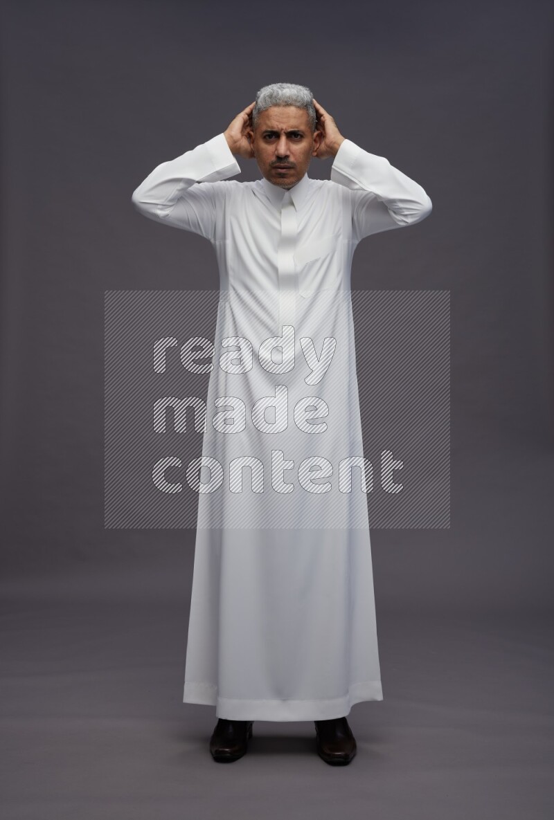 Saudi man wearing thob standing hands behind head on gray background
