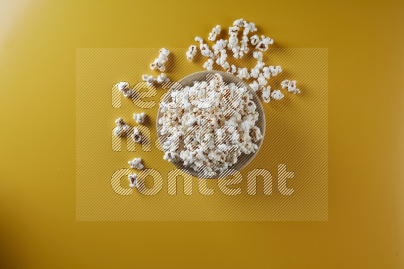 A multicolored ceramic plate full of popcorn with popcorn beside it on a yellow background in different angles