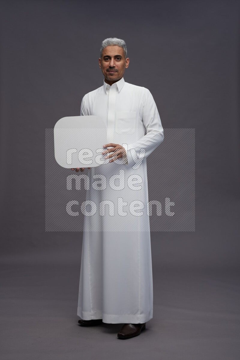 Saudi man wearing thob standing holding social media sign on gray background