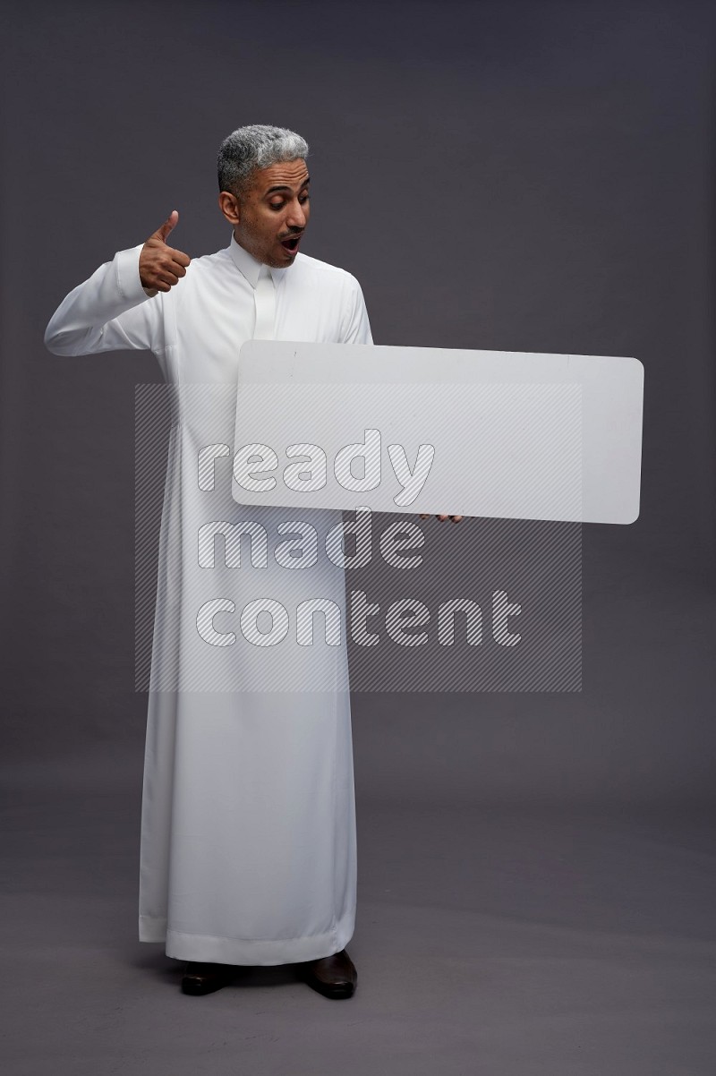 Saudi man wearing thob standing holding board on gray background