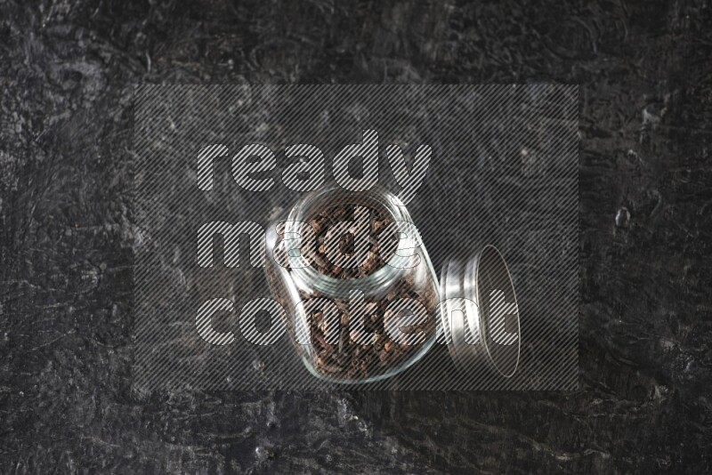 A glass spice jar full of cloves on textured black flooring