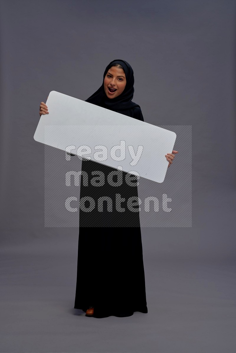 Saudi woman wearing Abaya standing holding white board on gray background