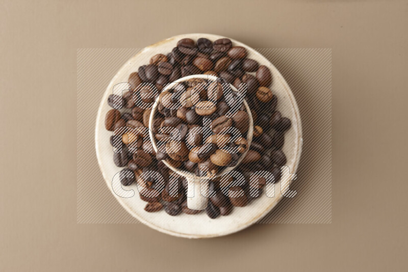 A beige pottery cup full of roasted coffee beans on beige background