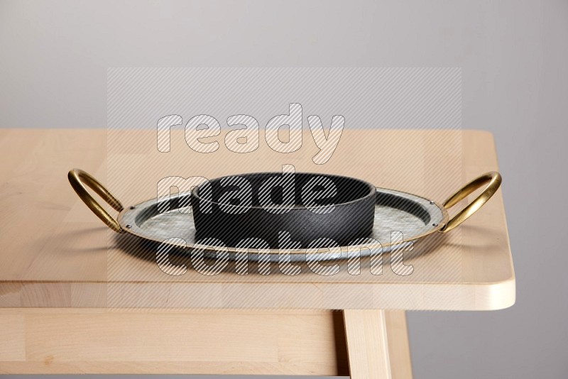 black bowl placed on a rounded stainless steel tray with golden handels on the edge of wooden table