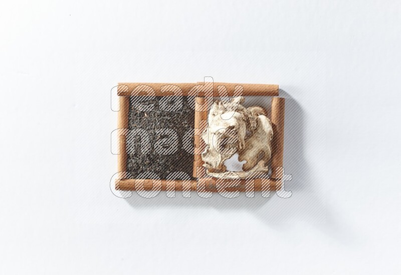 مربعان من أعواد القرفة ممتلئان بالشاي الأسود والزنجبيل المجفف علي خلفية بيضاء