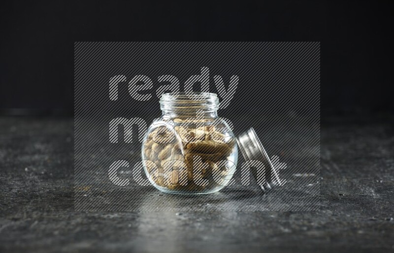 وعاء زجاجي للتوابل ممتلئ بأصابع الكركم المجففة على خلفية سوداء