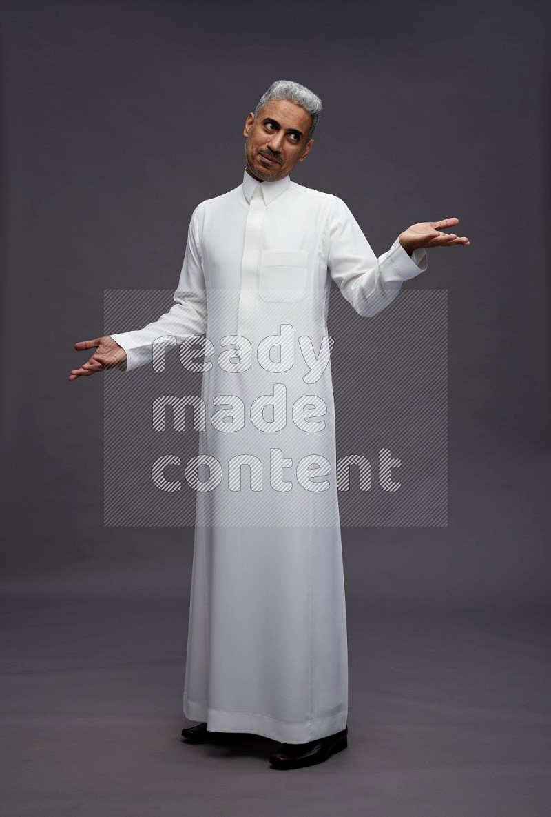 Saudi man wearing thob standing interacting with the camera on gray background