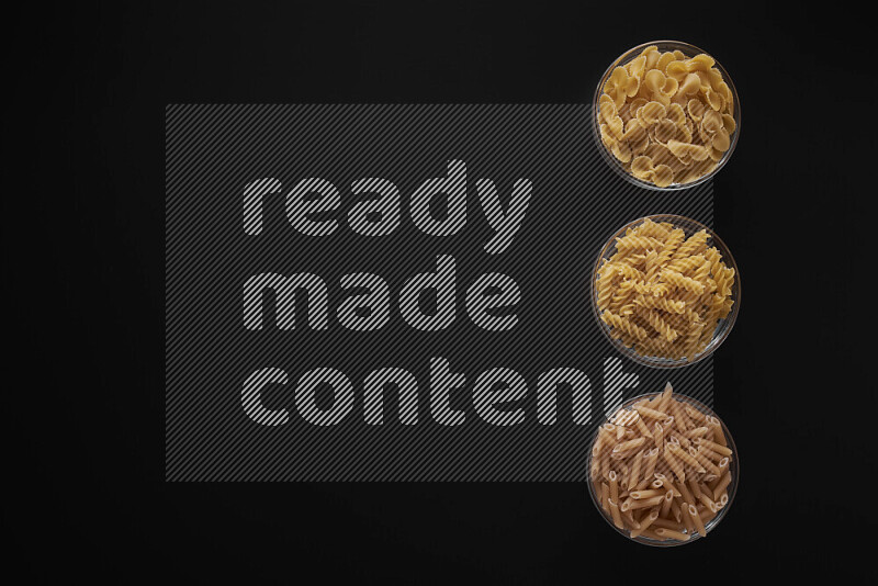 Different pasta types in 3 glass bowls on black background