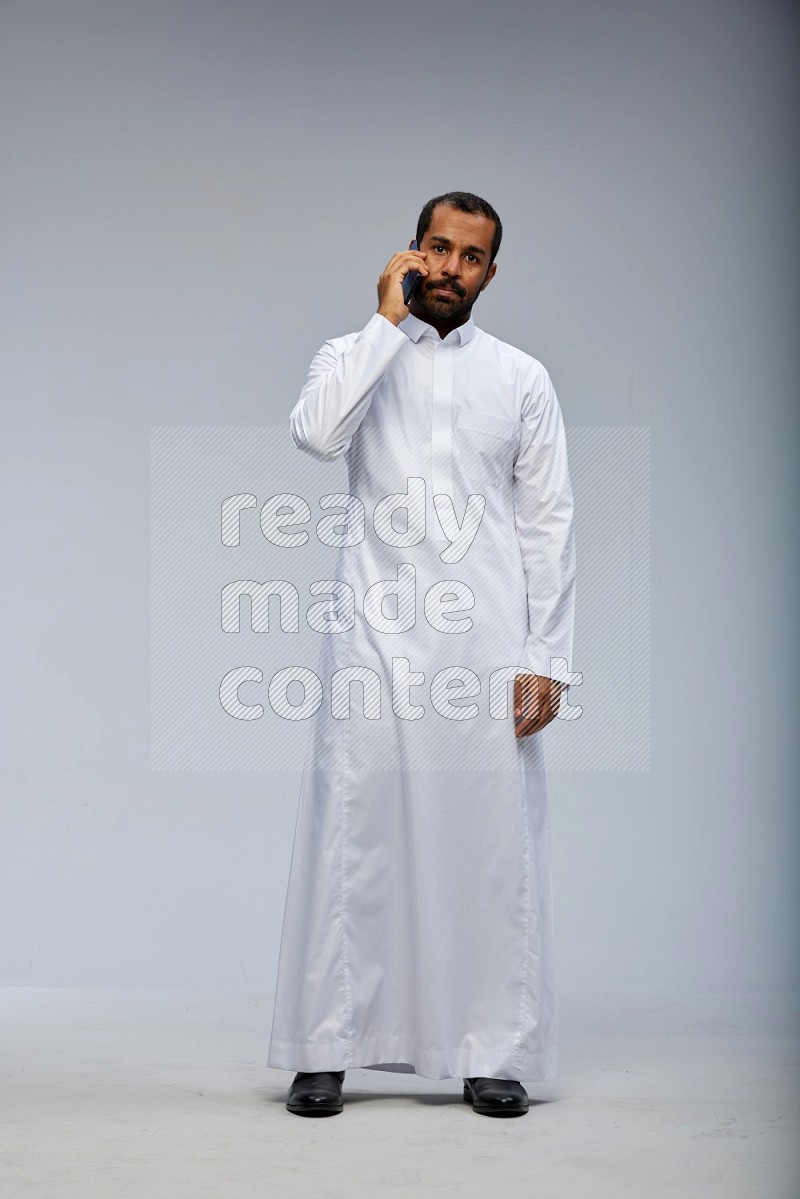 Saudi man wearing Thob standing talking on phone on Gray background