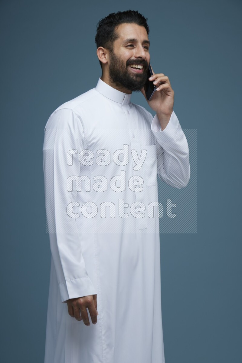 A man having a call on a blue background wearing Saudi Thob