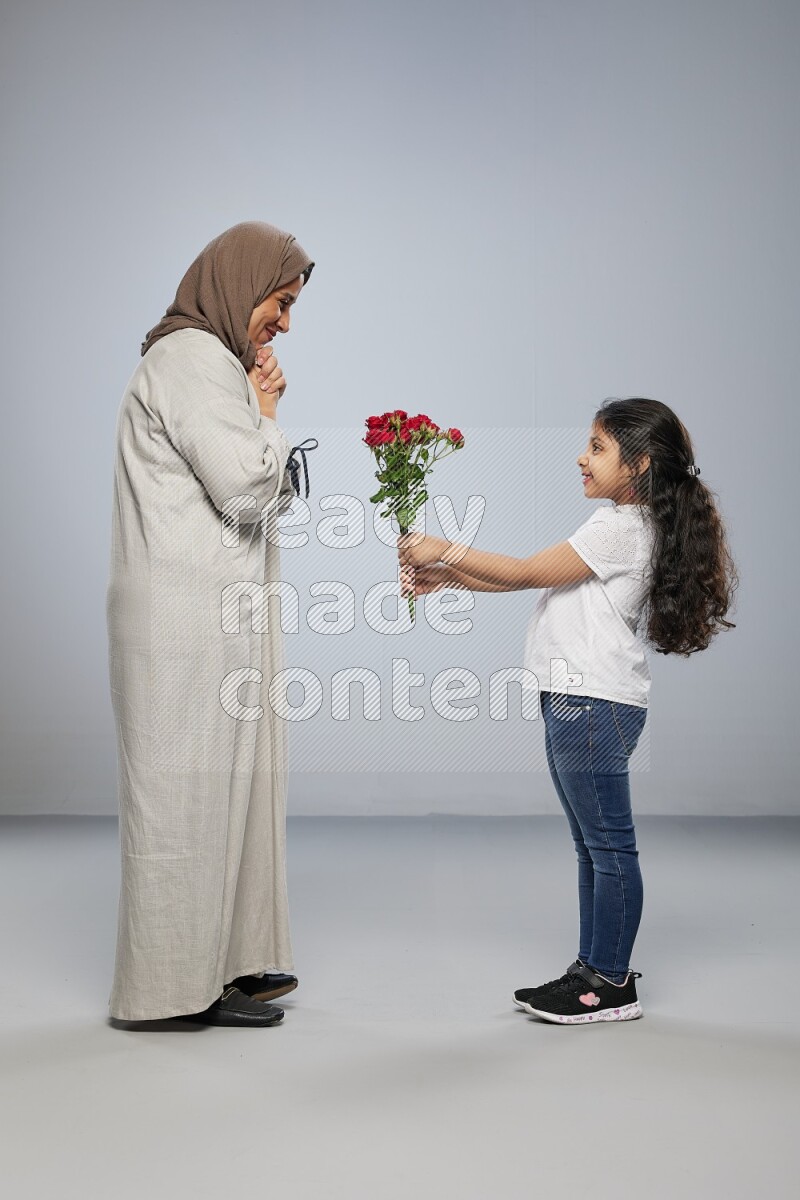 A girl standing giving flowers to her mother on gray background