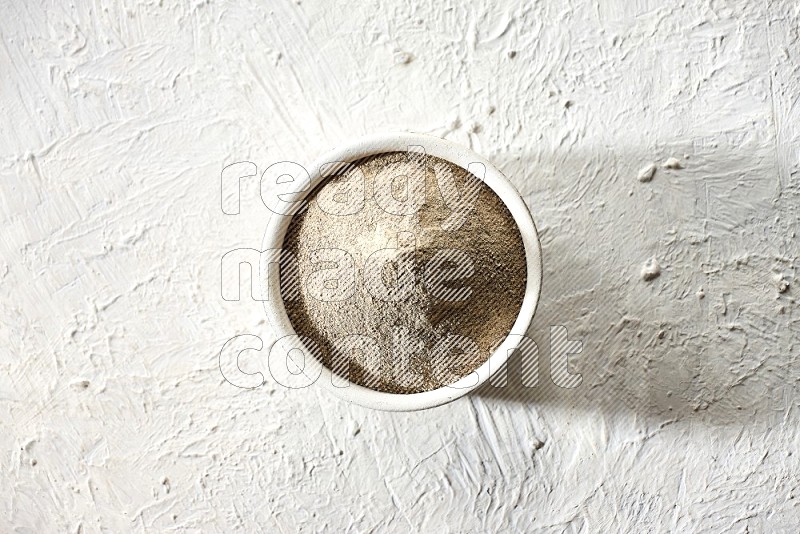 white pottery bowl full of white pepper powder on textured white flooring