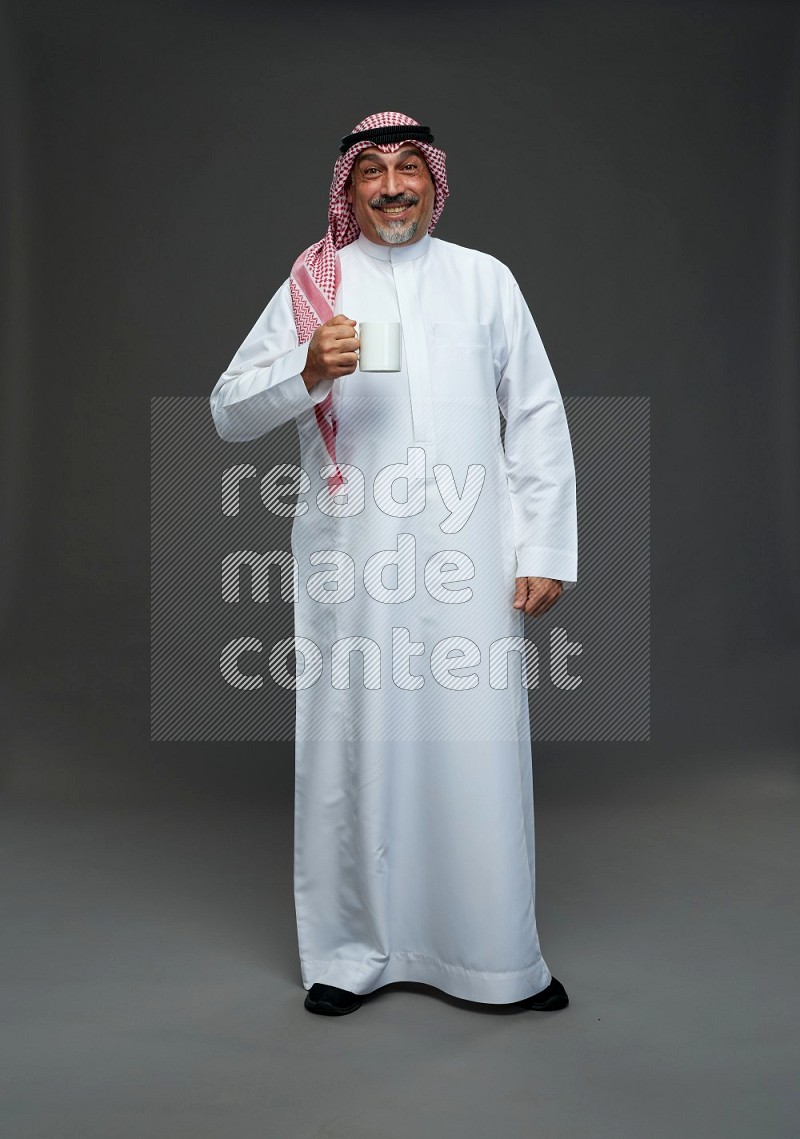 Saudi man with shomag Standing holding mug on gray background