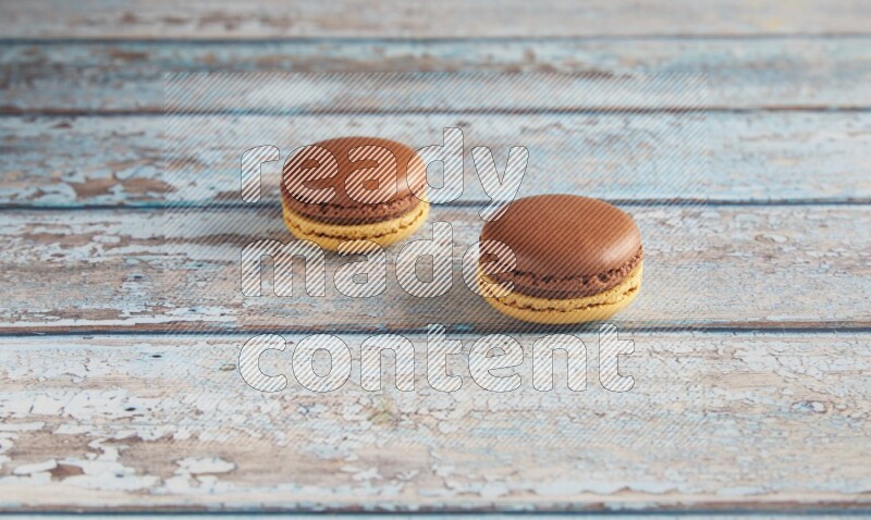 45º Shot of two Yellow and Brown Chai Latte macarons on light blue wooden background