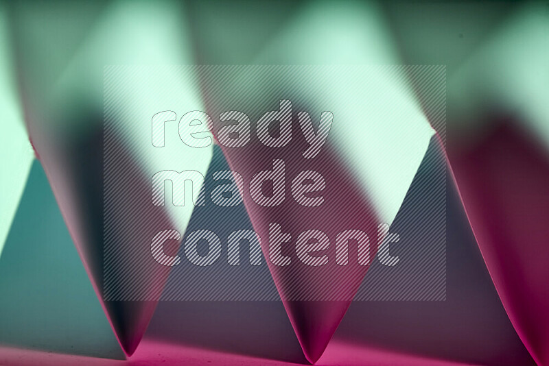 A close-up abstract image showing sharp geometric paper folds in green and pink gradients