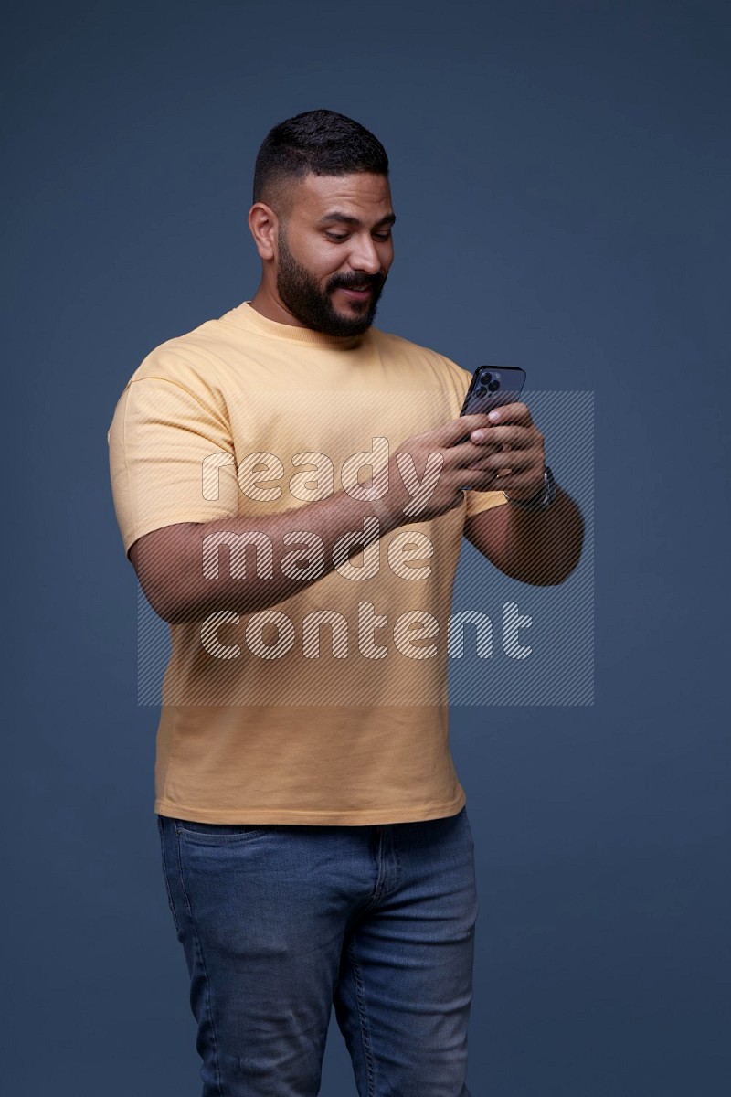 A man Texting on his phone on Blue Background wearing Orange T-shirt