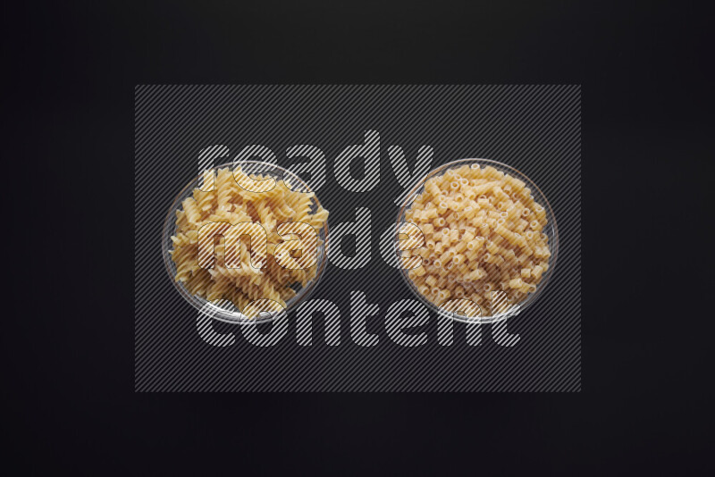 Different pasta types in glass bowls on black background