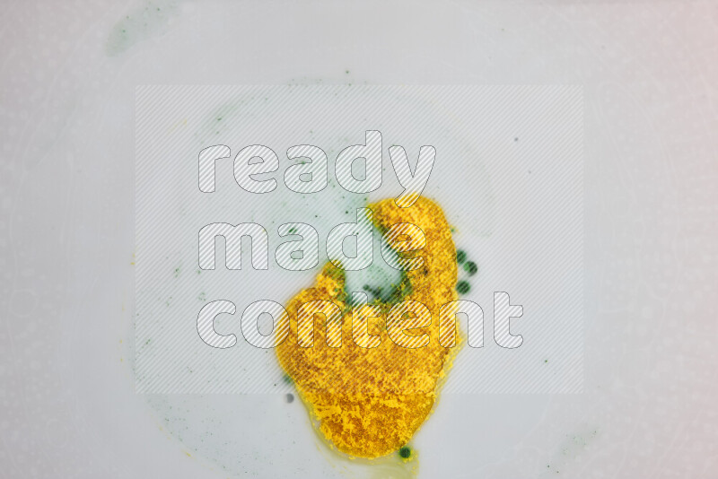 The image captures a splatter of yellow and green paint over a white backdrop