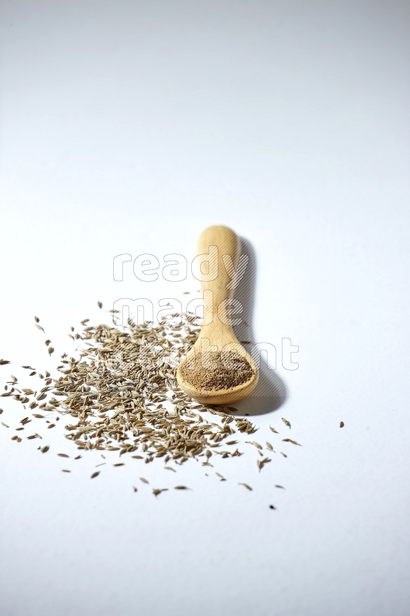 A wooden spoon full of cumin powder and cumin seeds beside it on white flooring