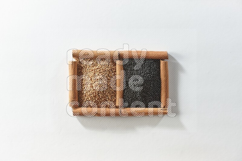 مربعان من أعواد القرفة ممتلئان بحبوب الخردل وحبة البركة السوداء علي خلفية بيضاء