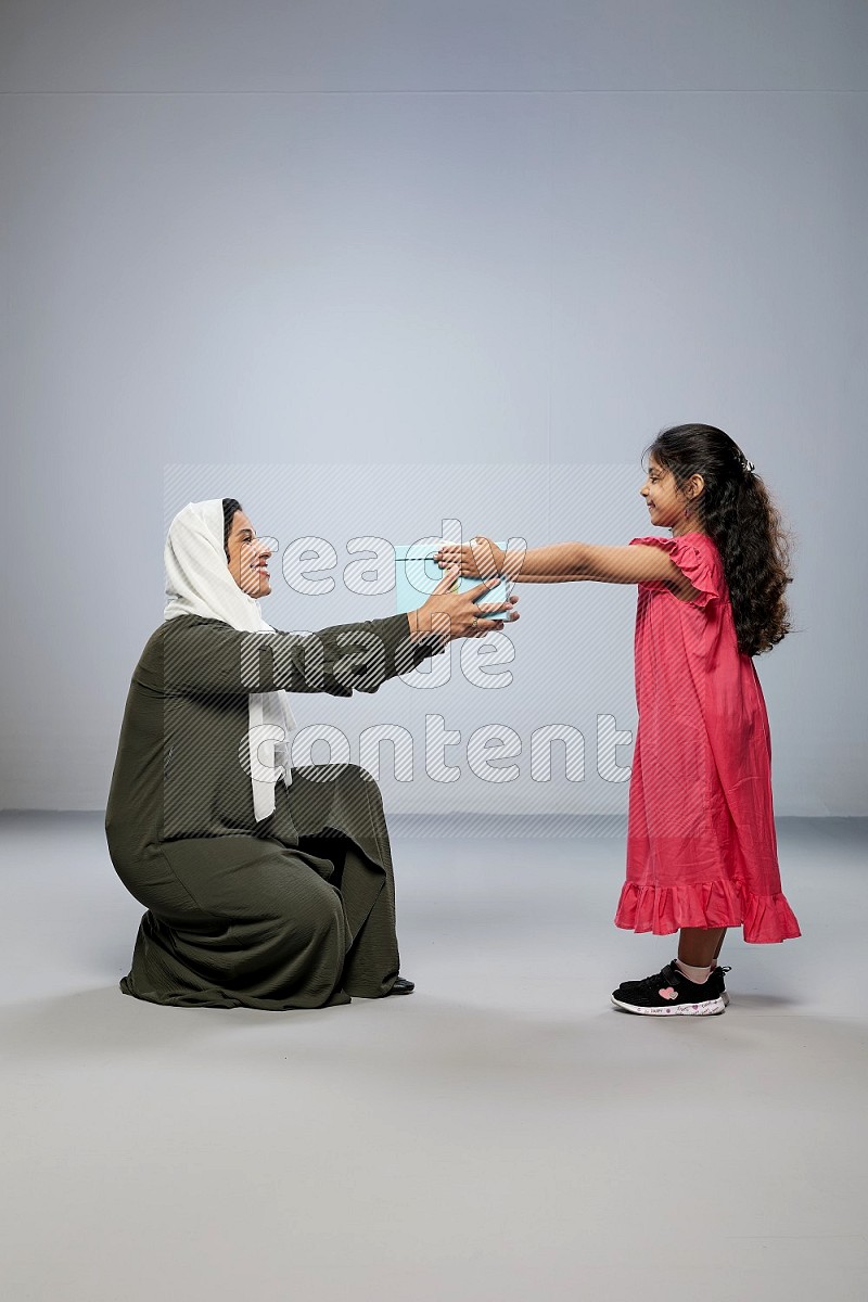 A girl giving a gift to her mother on gray background