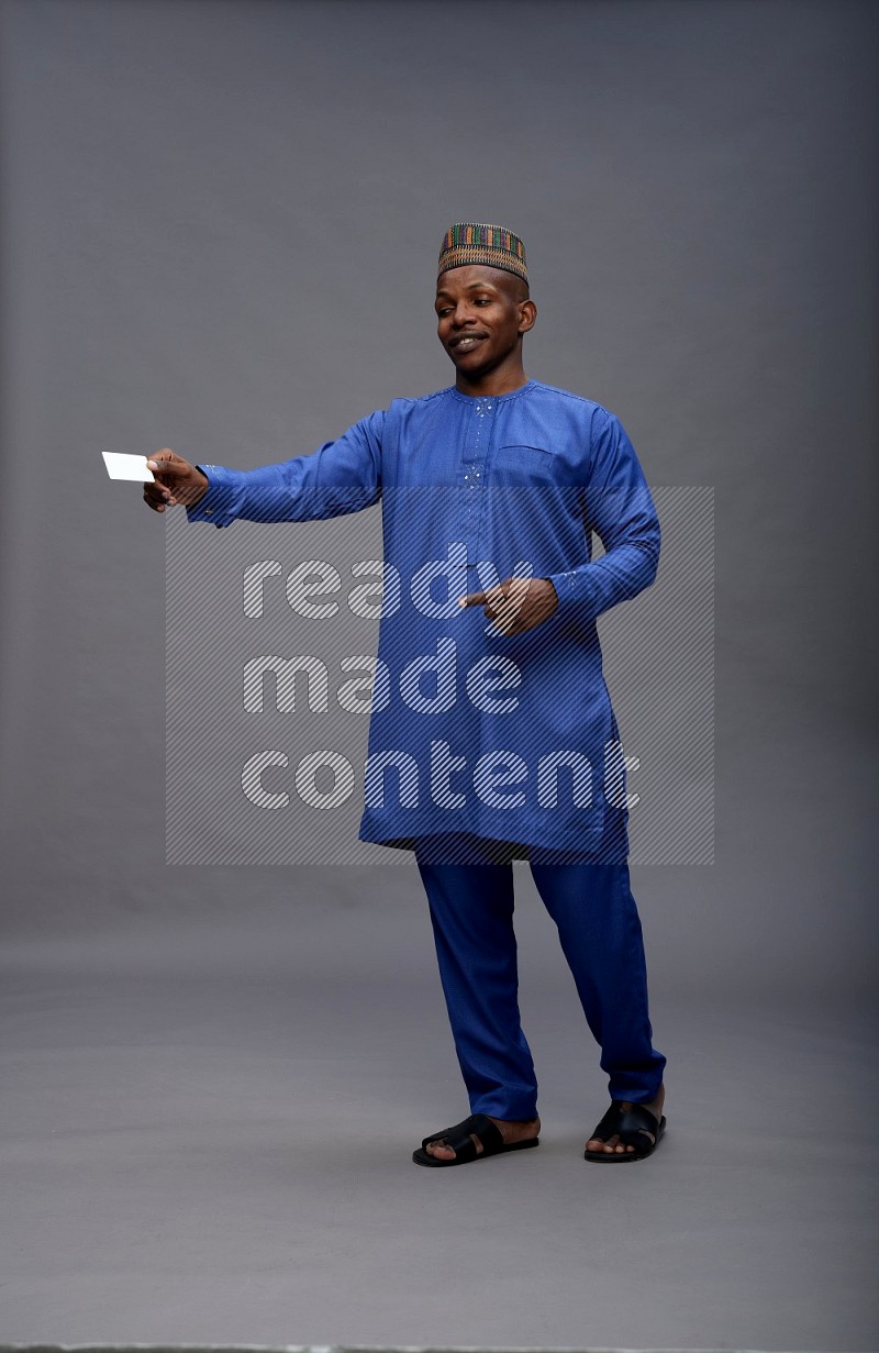 Man wearing Nigerian outfit standing holding ATM card on gray background