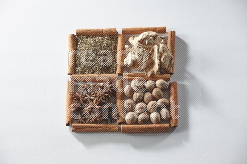 4 مربعات من أعواد القرفة ممتلئة باليانسون والزنجبيل والكمون وجوزة الطيب على أرضية بيضاء