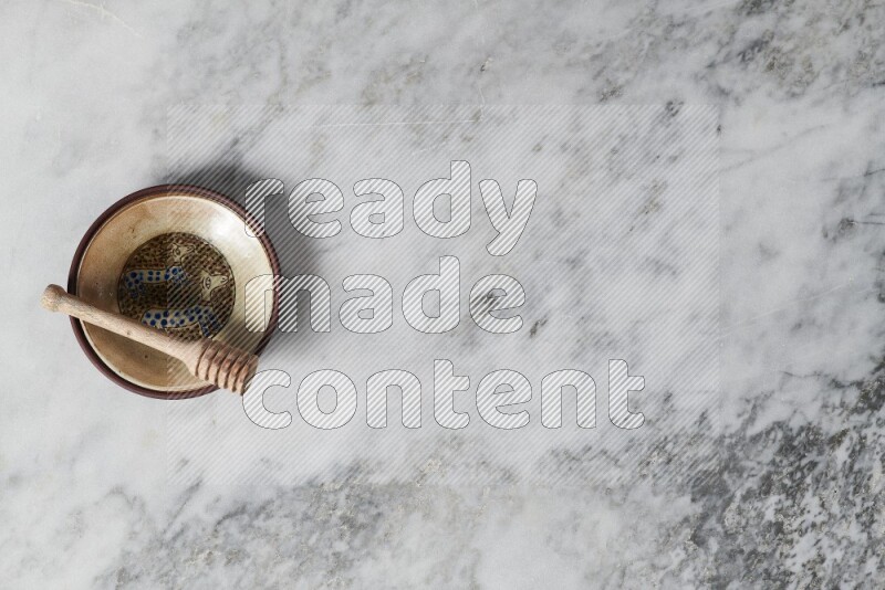 Decorative pottery plate with wooden honey dipper in it on grey marble background