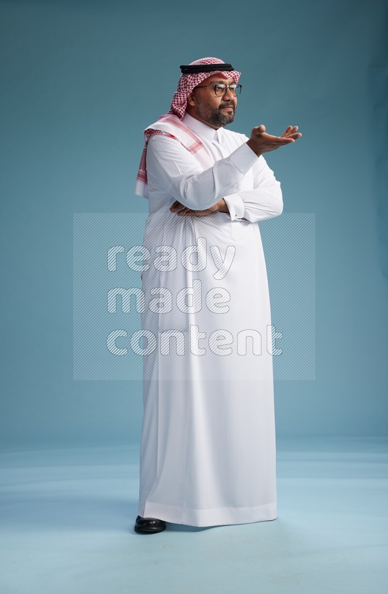 Saudi Man with shimag Standing Interacting with the camera on blue background