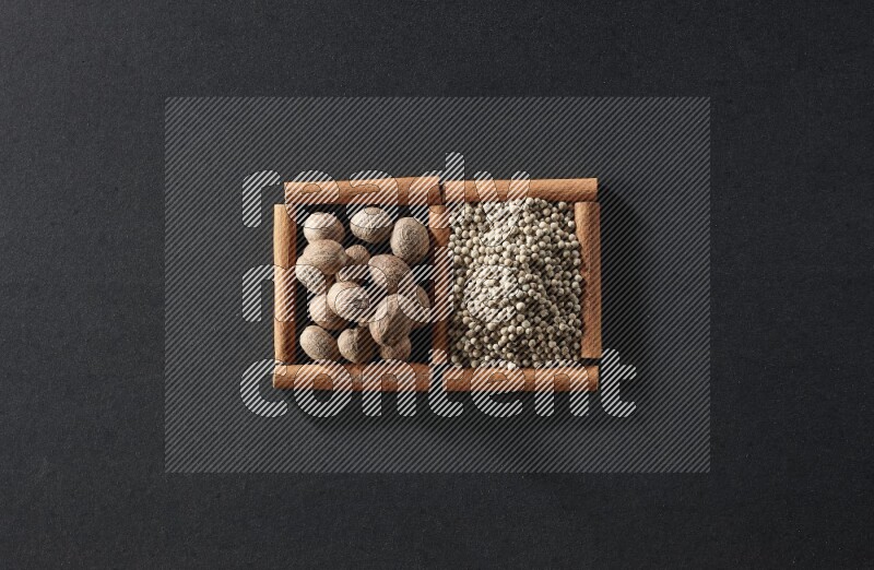 مربعان من أعواد القرفة ممتلئان بجوزة الطيب وحبوب الفلفل الأبيض علي خلفية سوداء