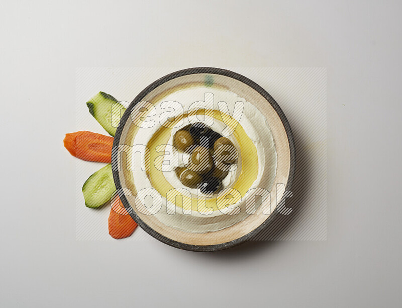 Lebnah garnished with whole black olives in a pottery plate on a white background
