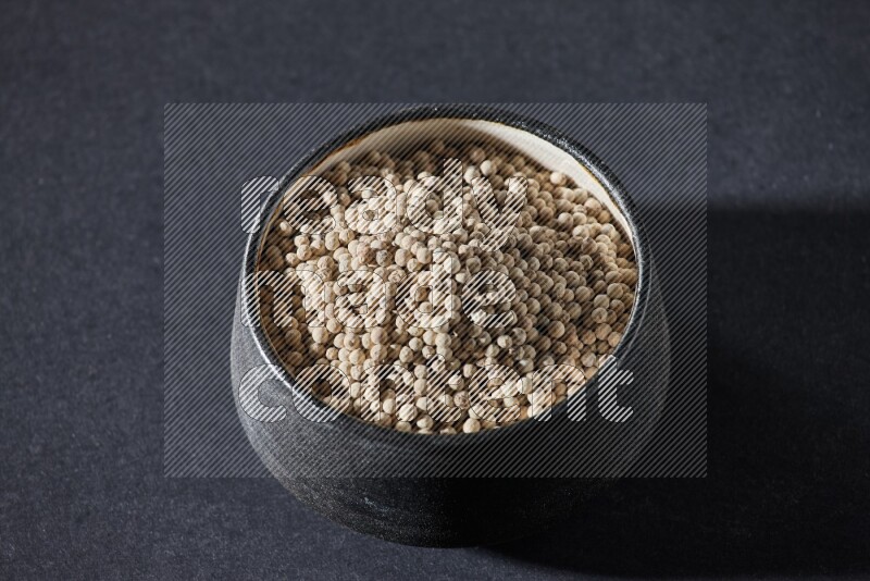 وعاء فخار أسود مملوء بالفلفل الأبيض على أرضية سوداء