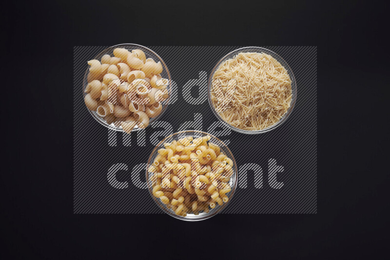 Different pasta types in glass bowls on black background