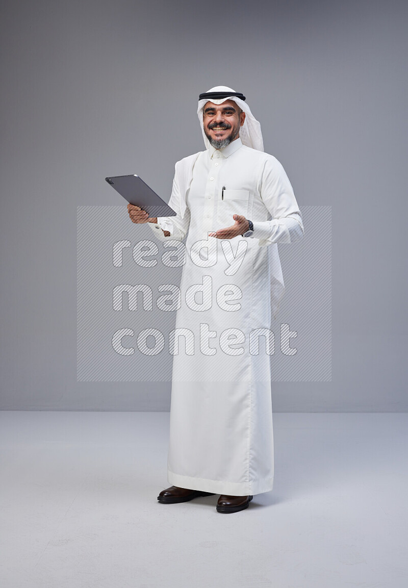 Saudi man Wearing Thob and white Shomag standing working on tablet on Gray background