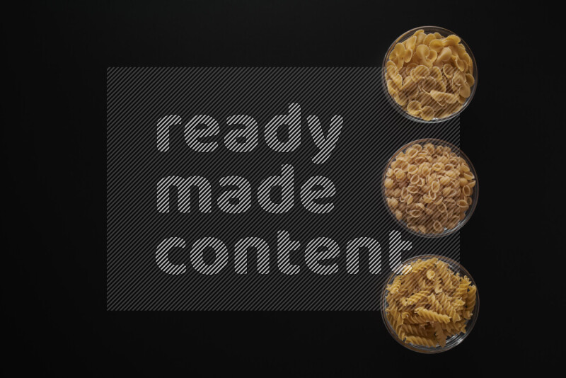 Different pasta types in 3 glass bowls on black background