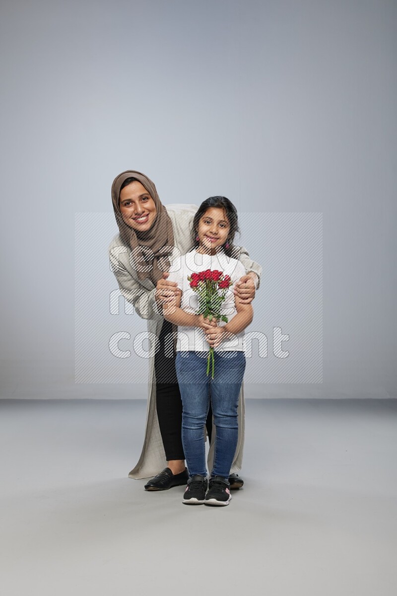 A girl standing giving flowers to her mother on gray background