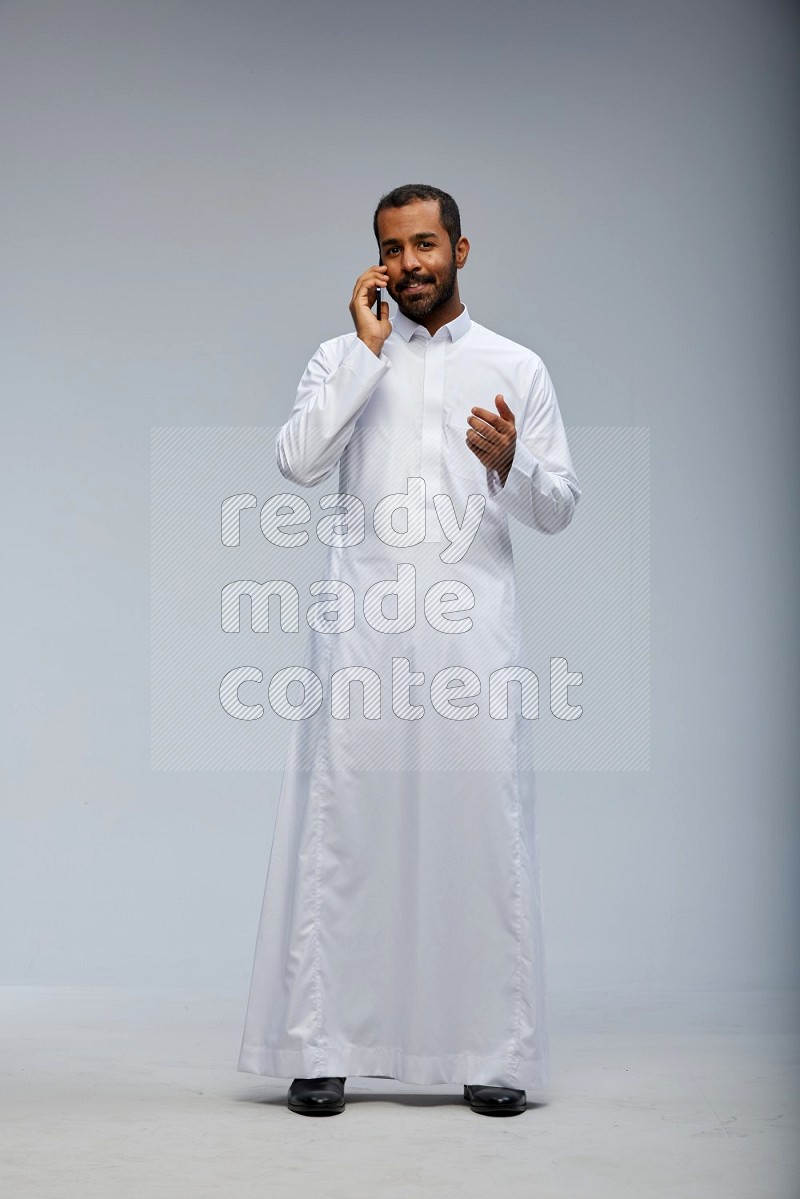 Saudi man wearing Thob standing talking on phone on Gray background