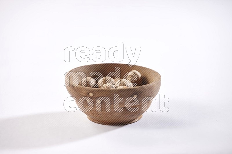 A wooden bowl full of whole nutmeg seeds on a white flooring