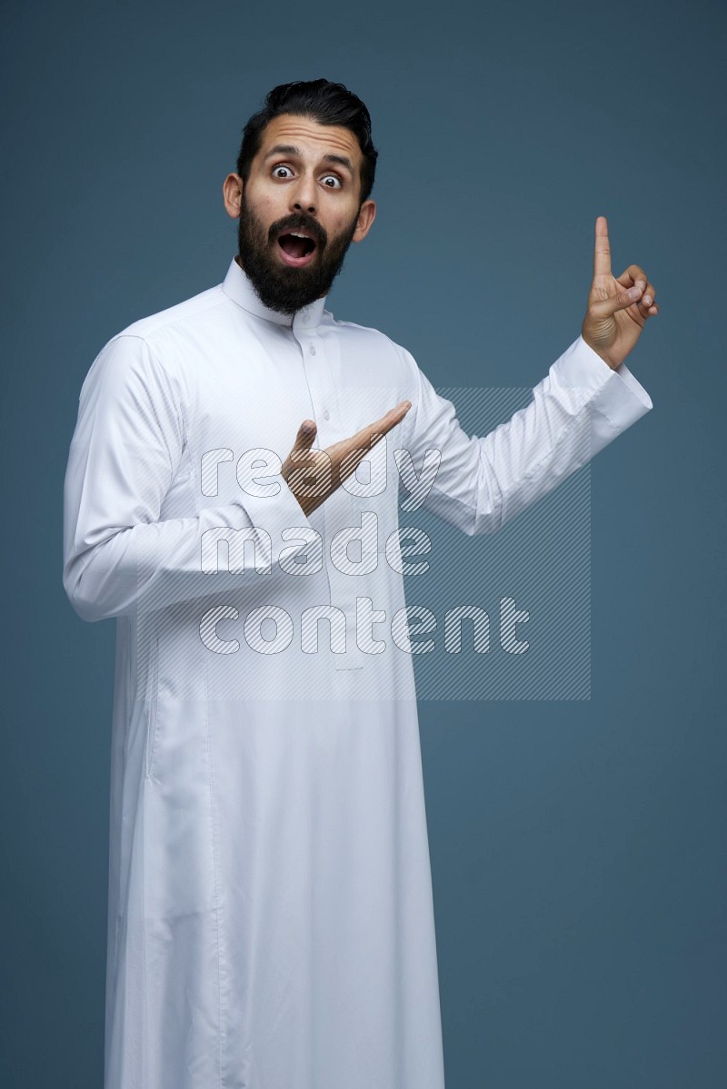 A man pointing in a blue background wearing Saudi Thob