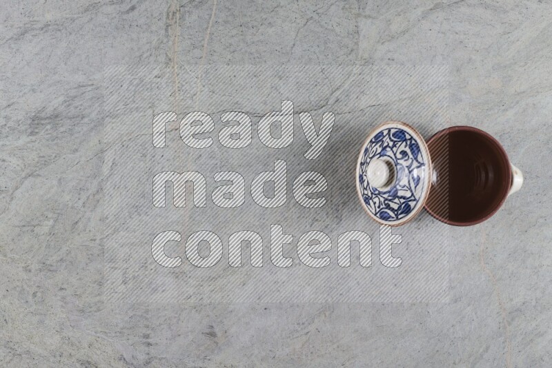 A multicolored pottery pot with its lid on grey marble background