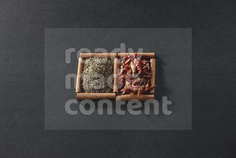 مربعان من أعواد القرفة ممتلئان بالفلفل الحار المجفف وحبوب الكمون علي خلفية سوداء