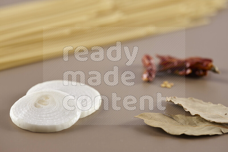 Raw pasta with different ingredients such as cherry tomatoes, garlic, onions, red chilis, black pepper, white pepper, bay laurel leaves, rosemary and cardamom on beige background