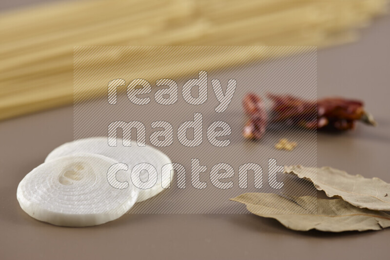 Raw pasta with different ingredients such as cherry tomatoes, garlic, onions, red chilis, black pepper, white pepper, bay laurel leaves, rosemary and cardamom on beige background