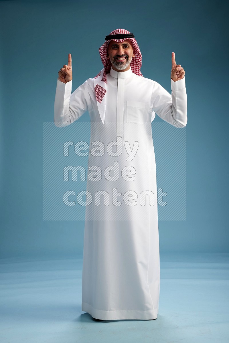 Saudi man wearing thob and shomagh posing to the camera on blue background