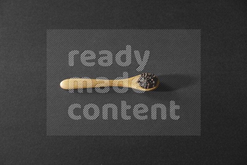 A wooden spoon full of black pepper on a black flooring