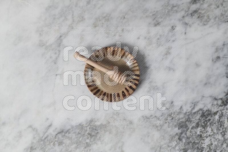Multicolored pottery plate with wooden honey dipper in it on grey marble background