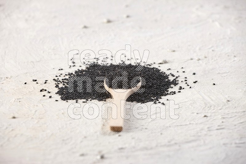 A wooden spoon full of black seeds on textured white flooring