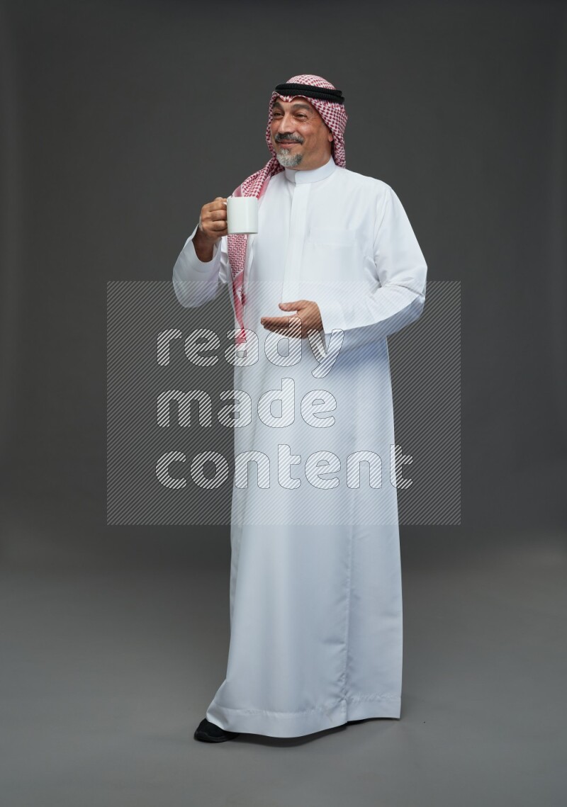 Saudi man with shomag Standing holding mug on gray background